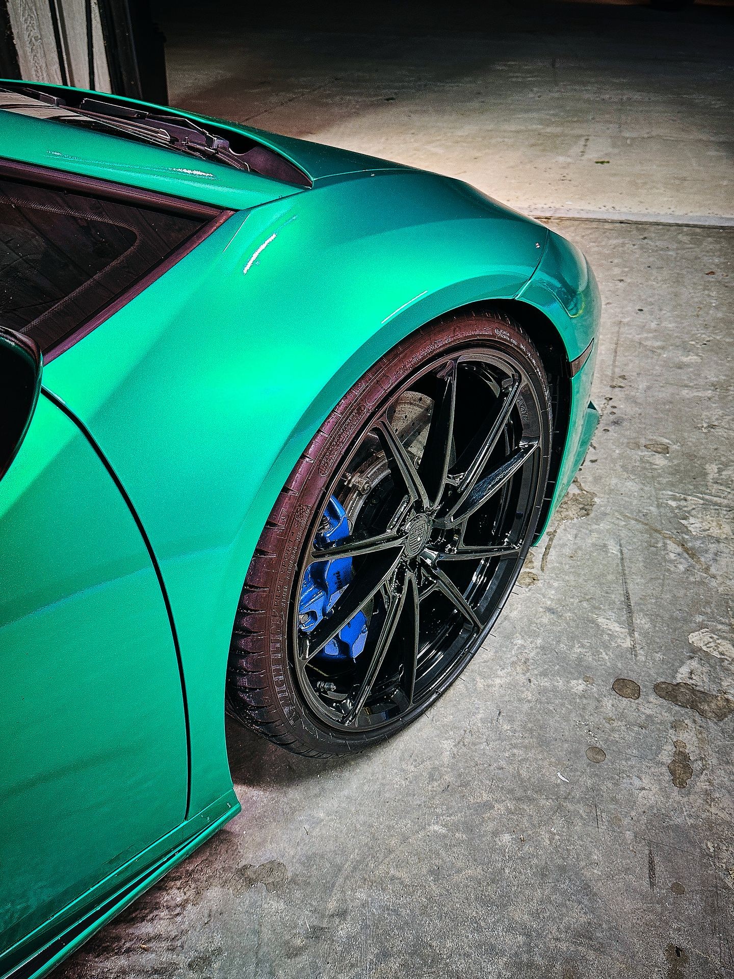 Close-up of a green sports car's front fender and black wheel on a concrete floor.